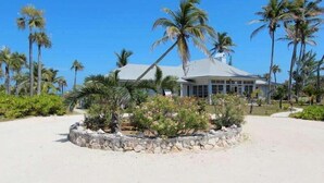 Une propriété située en bord de mer, avec une grande maison, des palmiers et une plage de sable.