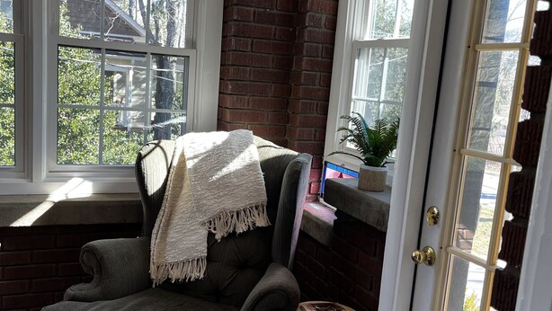 A cozy corner with a dark armchair, a small wooden stool, and a window seat with a brick wall and string lights.