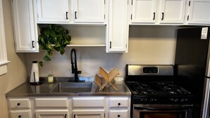 A kitchen with white cabinets, a stainless steel sink, a black faucet, a wooden cutting board, and a black stove.