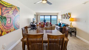 A dining area with a ceiling fan, a large painting, and a view of the ocean. - Ocean Sands 1107: Amazing Gulf Front Retreat (Madeira Beach)