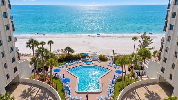 A hotel with a swimming pool, beach view, and palm trees. - Ocean Sands 1107: Amazing Gulf Front Retreat (Madeira Beach)