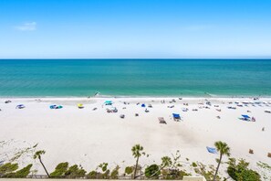 A beach with white sand, clear blue water, and a few palm trees.
