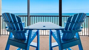 A balcony with two blue Adirondack chairs and a table, overlooking a clear blue sea. - Ocean Sands 1107: Amazing Gulf Front Retreat (Madeira Beach)