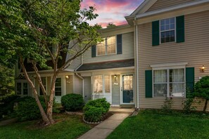 A two-story residential building with a front porch, a tree, and a well-maintained lawn. - BickelScape: Private Yard & Near DC (Sterling)