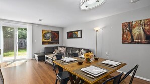 A dining area with a wooden table set for four, a sofa, and two paintings on the walls. - BickelScape: Private Yard & Near DC (Sterling)