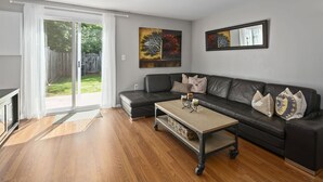 A living room with a black leather sofa, a wooden coffee table, and a sliding glass door leading to a backyard. - BickelScape: Private Yard & Near DC (Sterling)