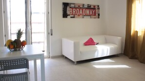 Un salon avec un canapé blanc, une petite table sur laquelle se trouve un panier de fruits, et un panneau mural sur lequel on peut lire « BROADWAY ».