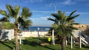 Un espace extérieur verdoyant, avec des palmiers, une clôture blanche et une vue sur la mer.