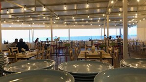 Un espace extérieur aménagé pour les repas, avec des tables et des chaises, offrant une vue sur la mer.