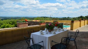 Una terraza con mesa preparada para tomar té, rodeada de plantas en macetas y una vista panorámica.