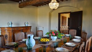 Comedor con mesa de madera dispuesta para una comida, rodeado de sillas de mimbre y un candelabro colgando del techo.