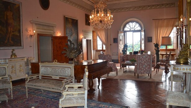 Una sala majestuosa con muebles elaborados, un piano de cola y una araña de cristal.
