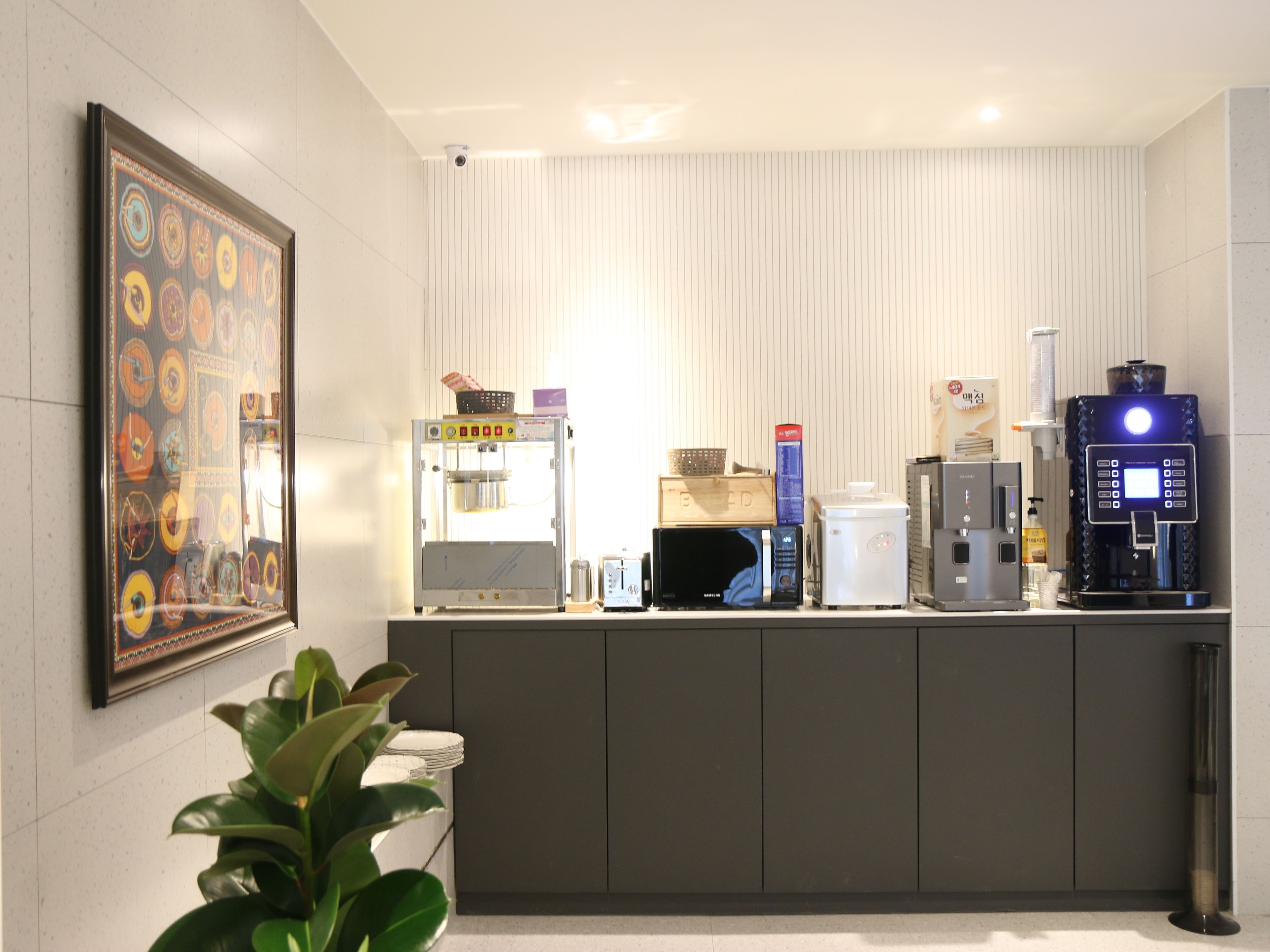 A modern kitchen area with a coffee machine, microwave, and a framed artwork on the wall.