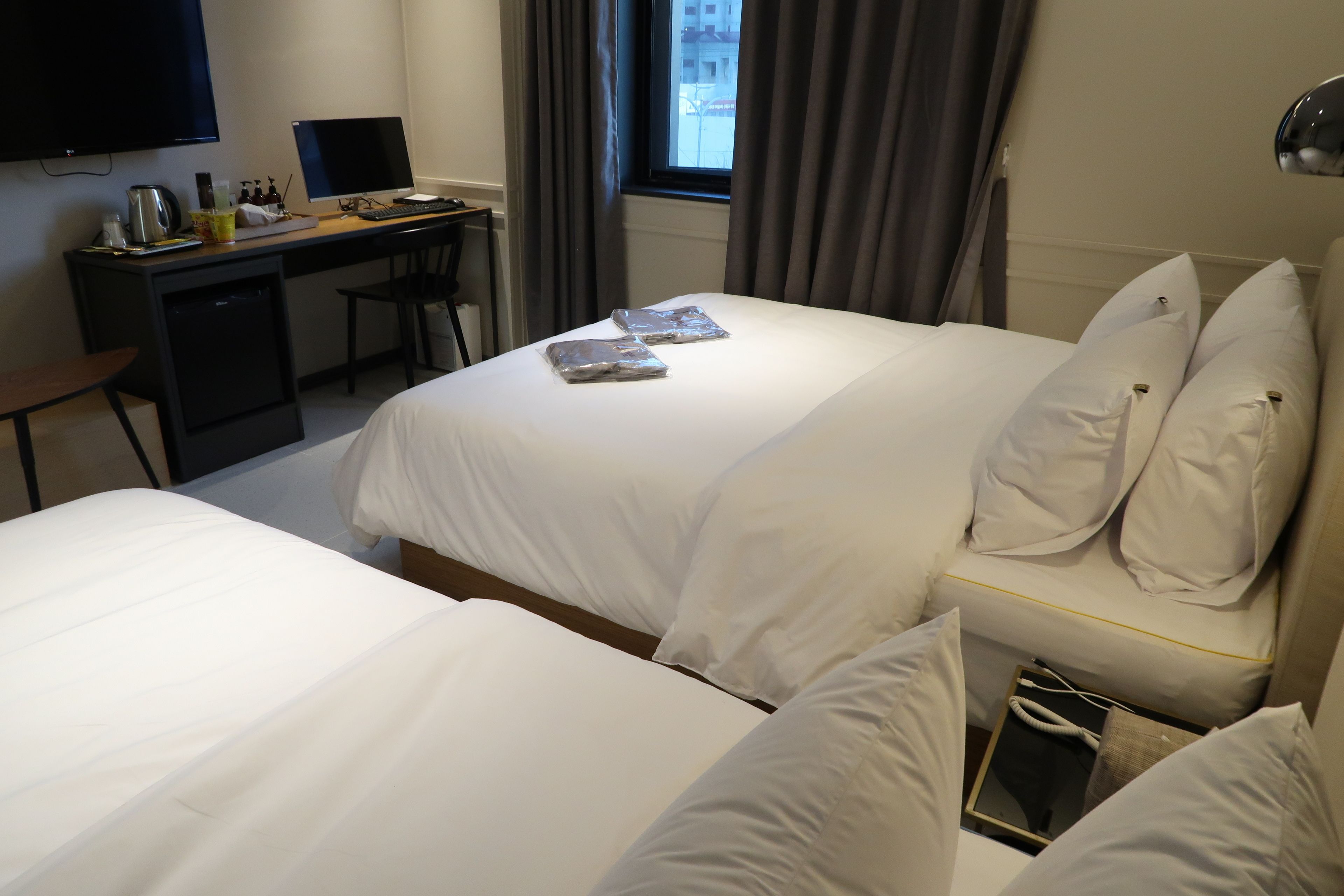 Una camera d'albergo con due letti, una scrivania con un computer e una televisione.
