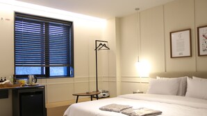 A hotel room with a bed, bedside table, lamp, and a window with blinds. - Brown dot Hotel Palyong (Changwon)