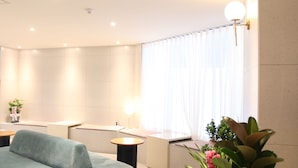 A modern, well-lit room with a sofa, a small table, and a large window with sheer curtains. - Brown dot Hotel Palyong (Changwon)