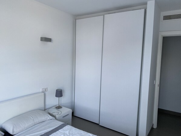 Quarto com cama, mesa de cabeceira, luminária e guarda-roupa.