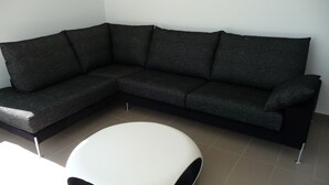 A modern living room with a dark grey sectional sofa and a white, round, minimalist coffee table. - Ground Floor With Stunning Sea Views And Private Terrace, Shared Pool (Pollença)