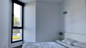 A bedroom with a large window, a bed with white bedding, a bedside table with a lamp, and a headboard with pillows. - Ground Floor With Stunning Sea Views And Private Terrace, Shared Pool (Pollença)