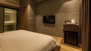 Une chambre d’hôtel moderne dotée d’un grand lit, d’un téléviseur à écran plat fixé au mur, d’un minibar et d’une porte en bois.