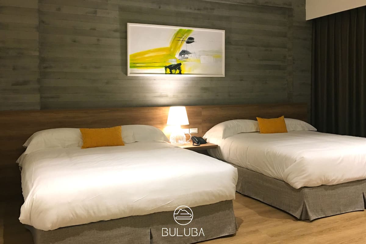 A hotel room with two beds, a wooden headboard, a painting on the wall, and a nightstand with a lamp and phone.