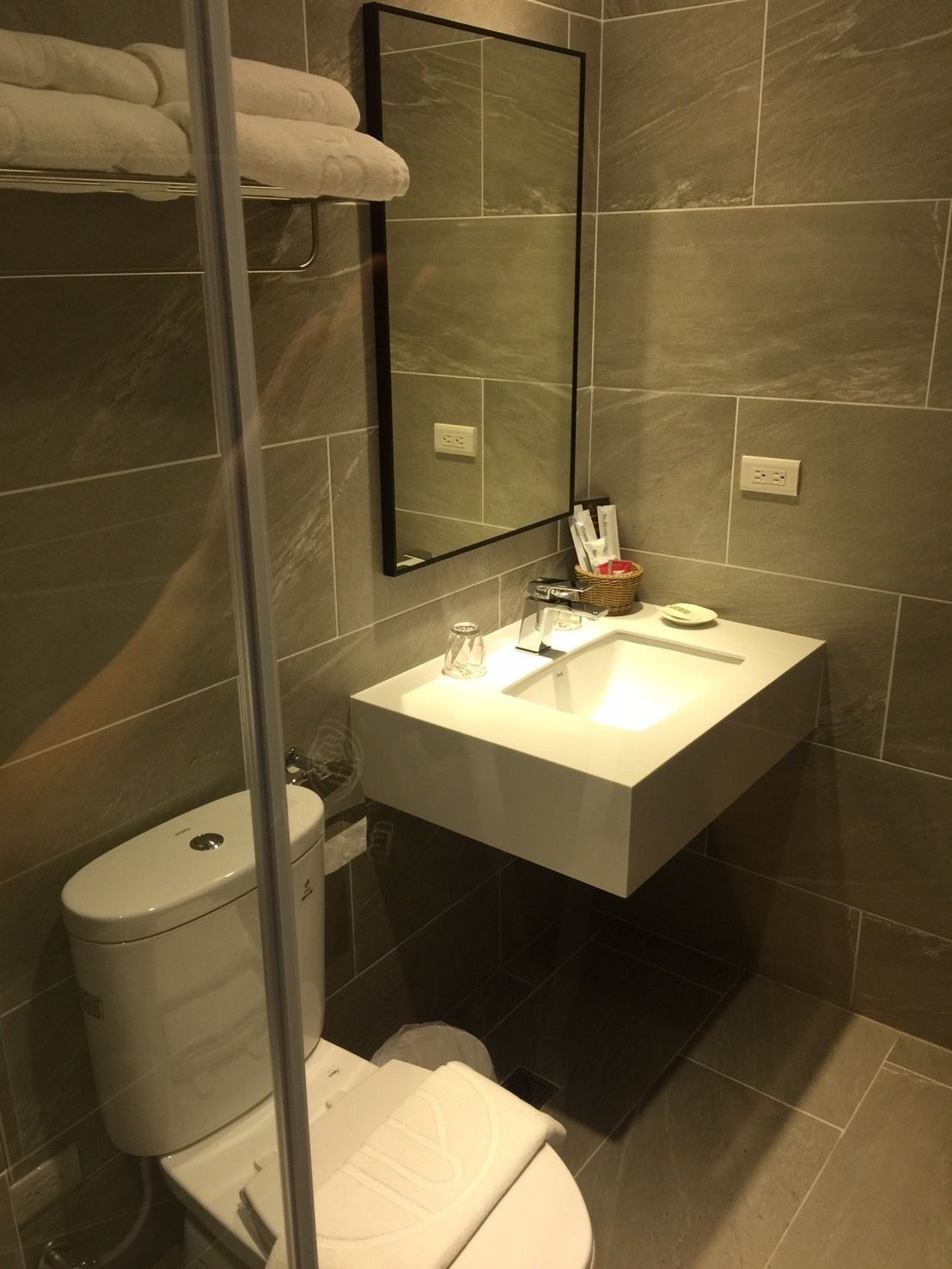 Uma casa de banho moderna com uma sanita, um lavatório branco e um espelho grande.