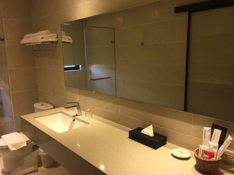 A modern bathroom with a large mirror, a sink, and a toilet. There are towels on a rack and a basket with toiletries.