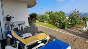 A balcony with lounge chairs and a table, overlooking a garden with trees and flowers. - House / Villa - Santa Cruz (Santa Cruz)