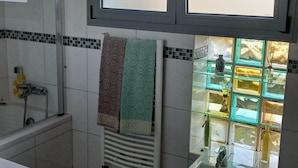 Une salle de bain avec une baignoire, un bidet, un porte-serviettes avec des serviettes à motifs, une fenêtre en verre dépoli et un sol carrelé.