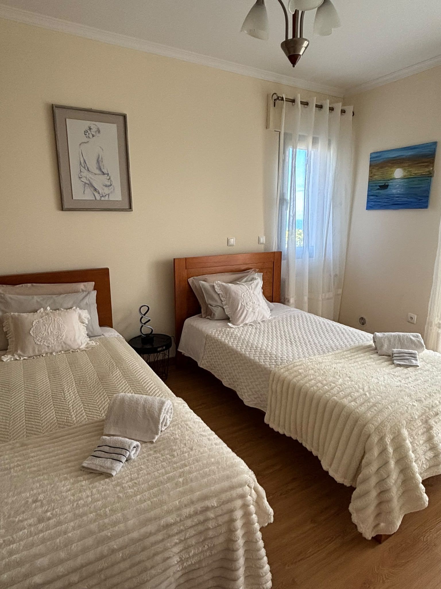 A hotel room with two beds, a painting on the wall, and a window with curtains.