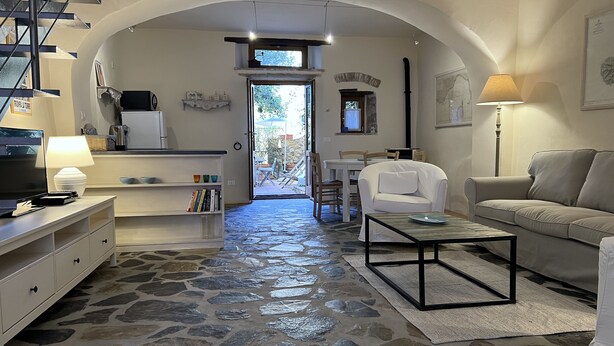 A cozy living room with a stone floor, a white sofa, a coffee table, and a TV on a wooden stand. - House with garden in the historical center House with character. (Capoliveri)