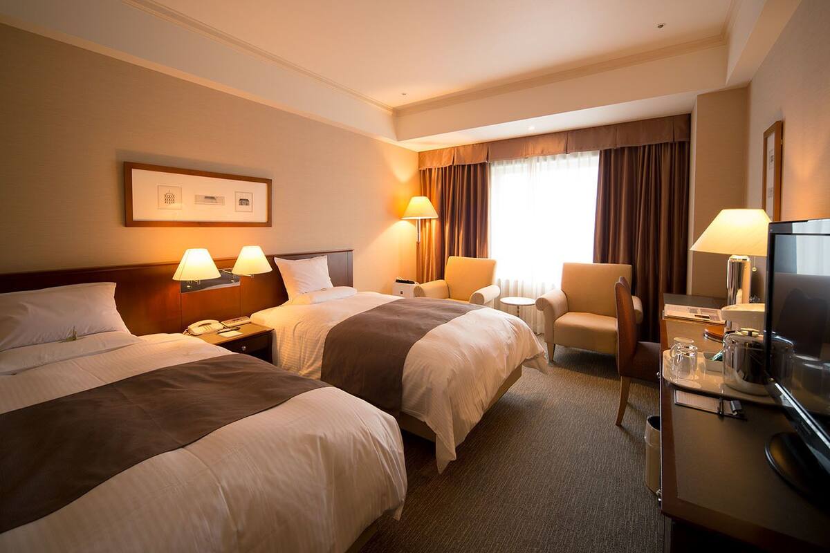 Une chambre d’hôtel avec deux lits, un bureau avec une télévision et une chaise.