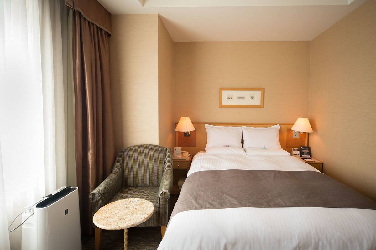 Une chambre d’hôtel comprenant un lit, deux lampes de chevet, une chaise, une petite table et un tableau accroché au mur.