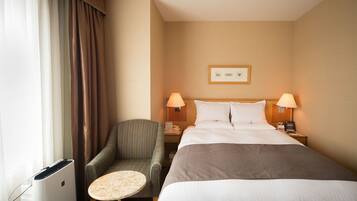 A hotel room with a bed, two bedside lamps, a chair, a small table, and a wall-mounted picture.