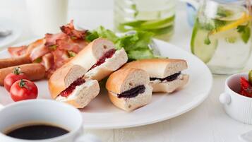Een bord met belegde broodjes, spek, tomaten en een kop koffie.