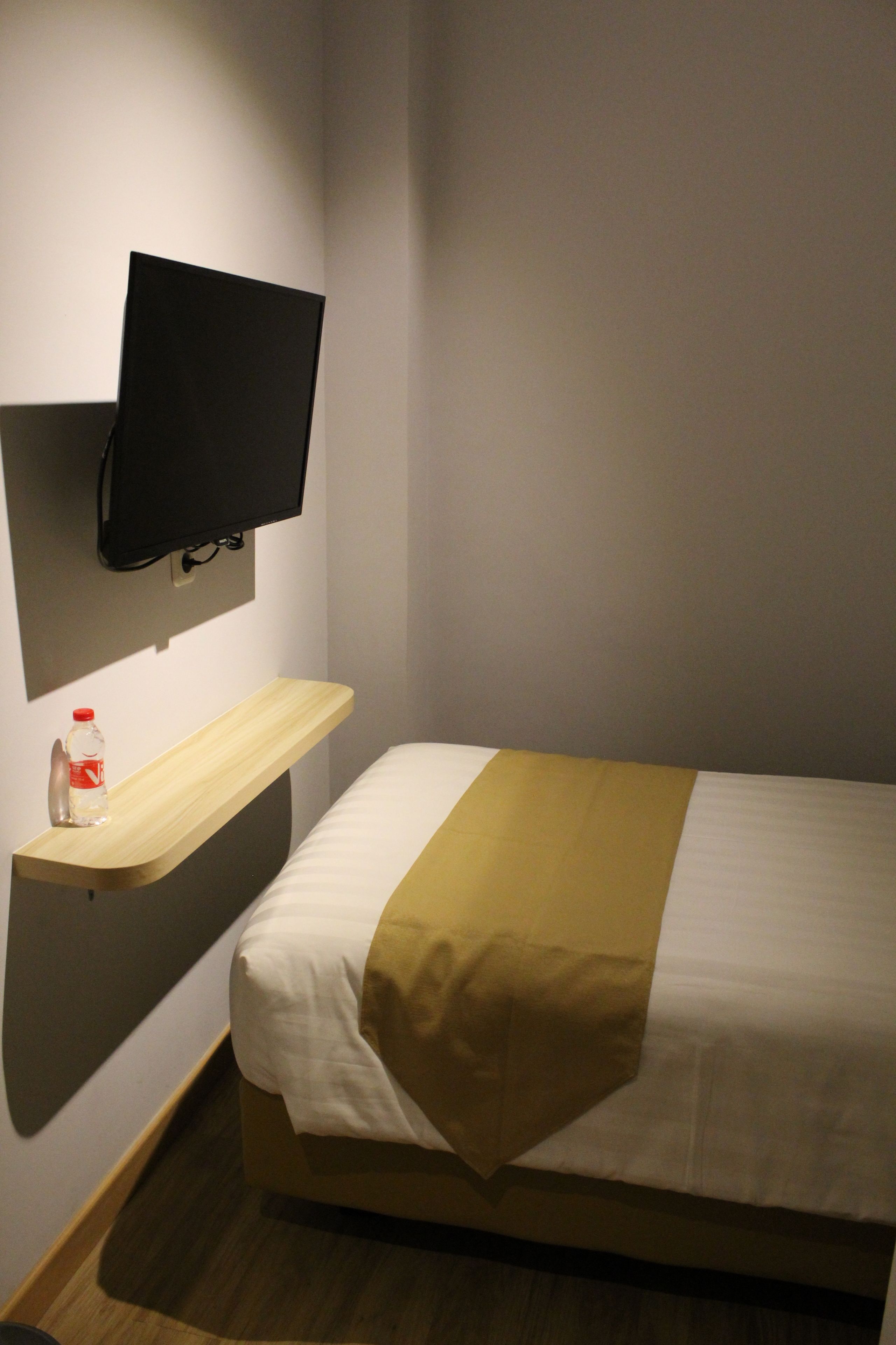Une chambre d’hôtel avec un lit, un téléviseur fixé au mur et une bouteille d’eau posée sur une étagère.