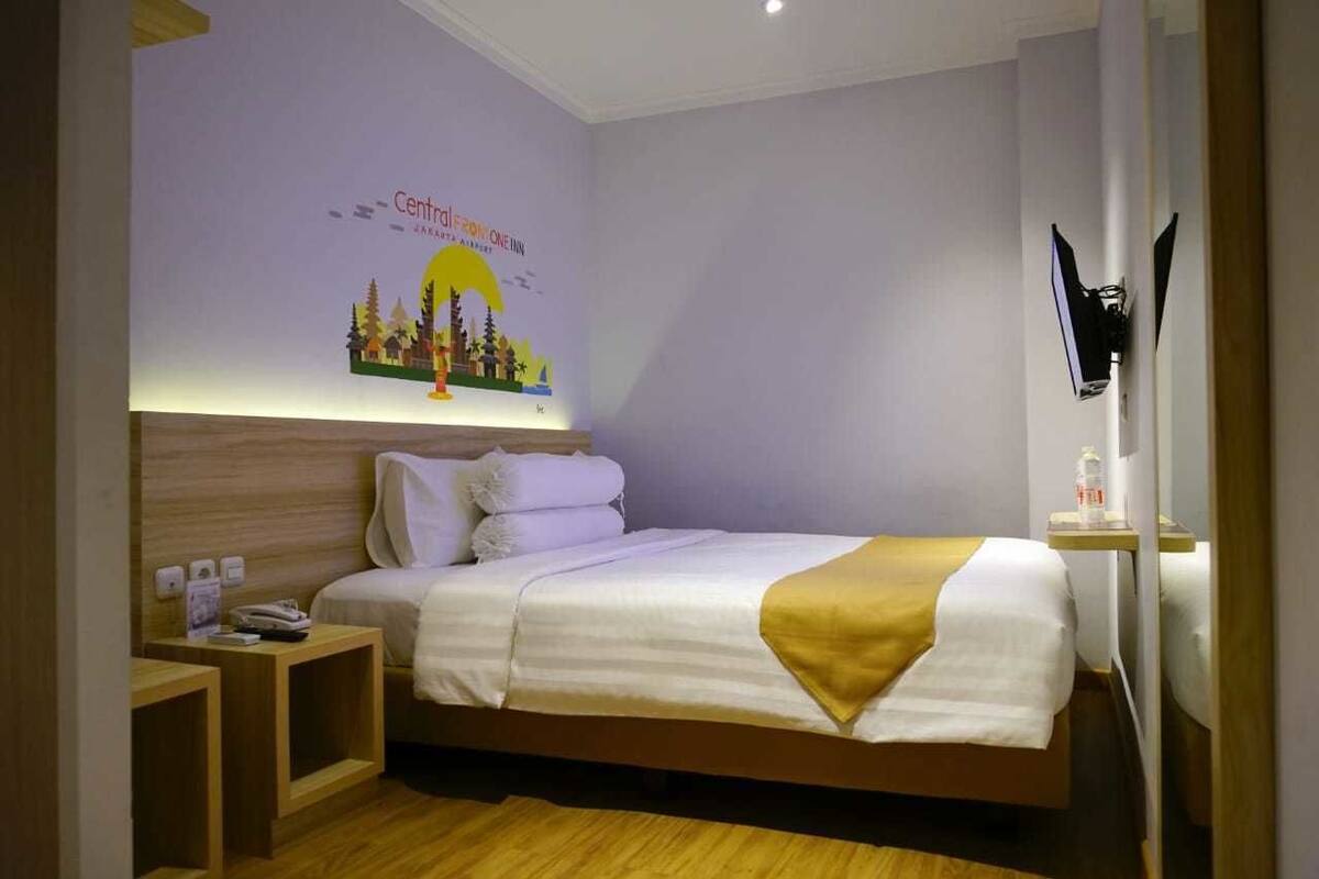 Habitación de hotel con una cama, mesitas de noche de madera, un televisor montado en la pared y un cartel en la pared.