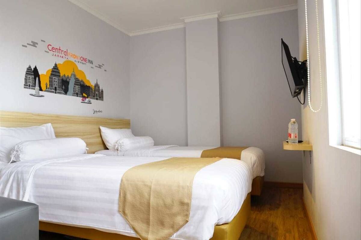 Habitación de hotel con dos camas, un televisor montado en la pared y una repisa con una botella.