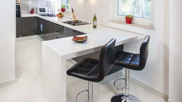 Una cucina moderna con mobili bianchi, un'isola centrale con sgabelli da bar, una finestra vista e un forno a microonde integrato.