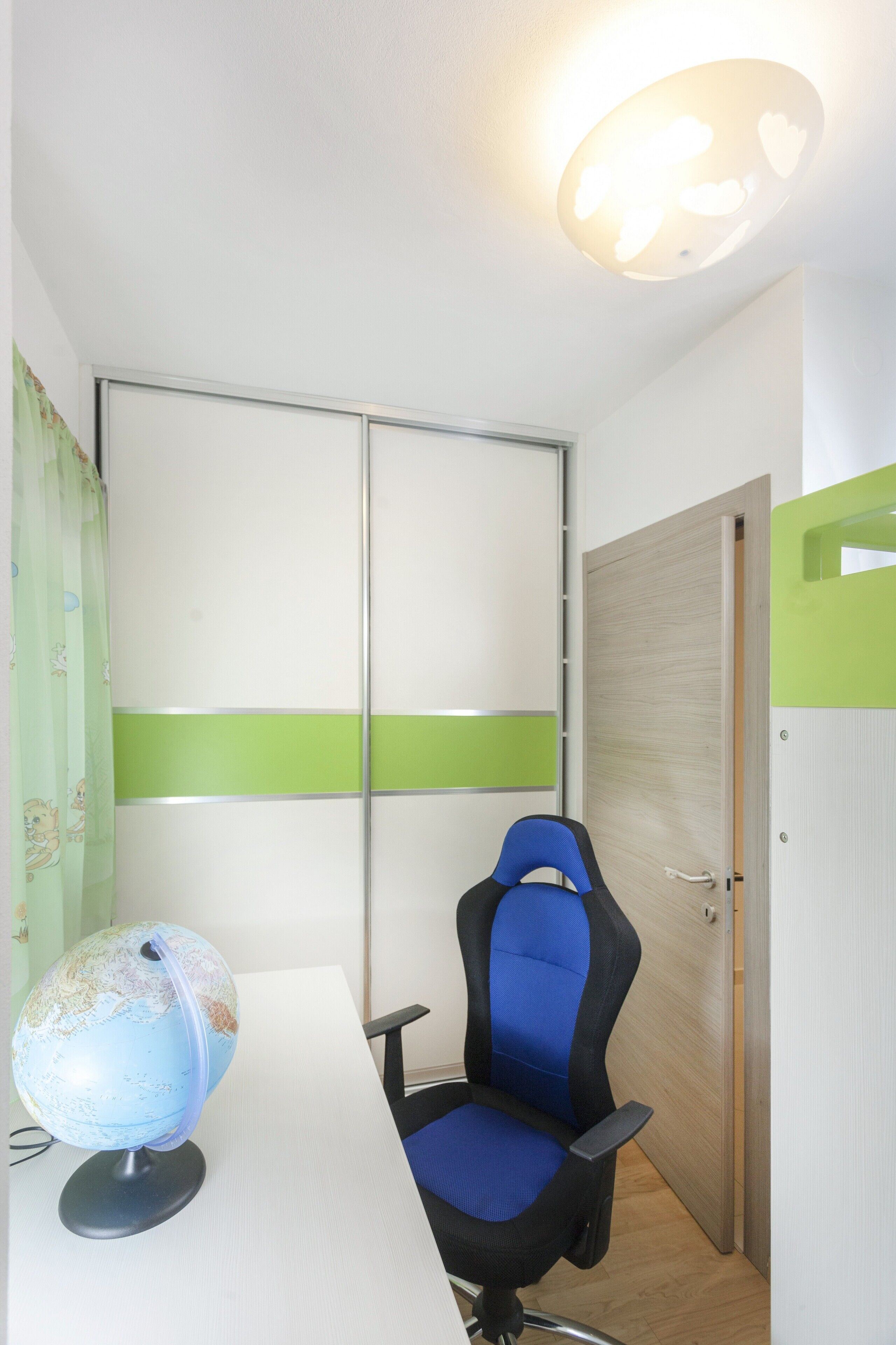 A room with a desk, a globe, a blue chair, a wooden door, and a green stripe on the wall.