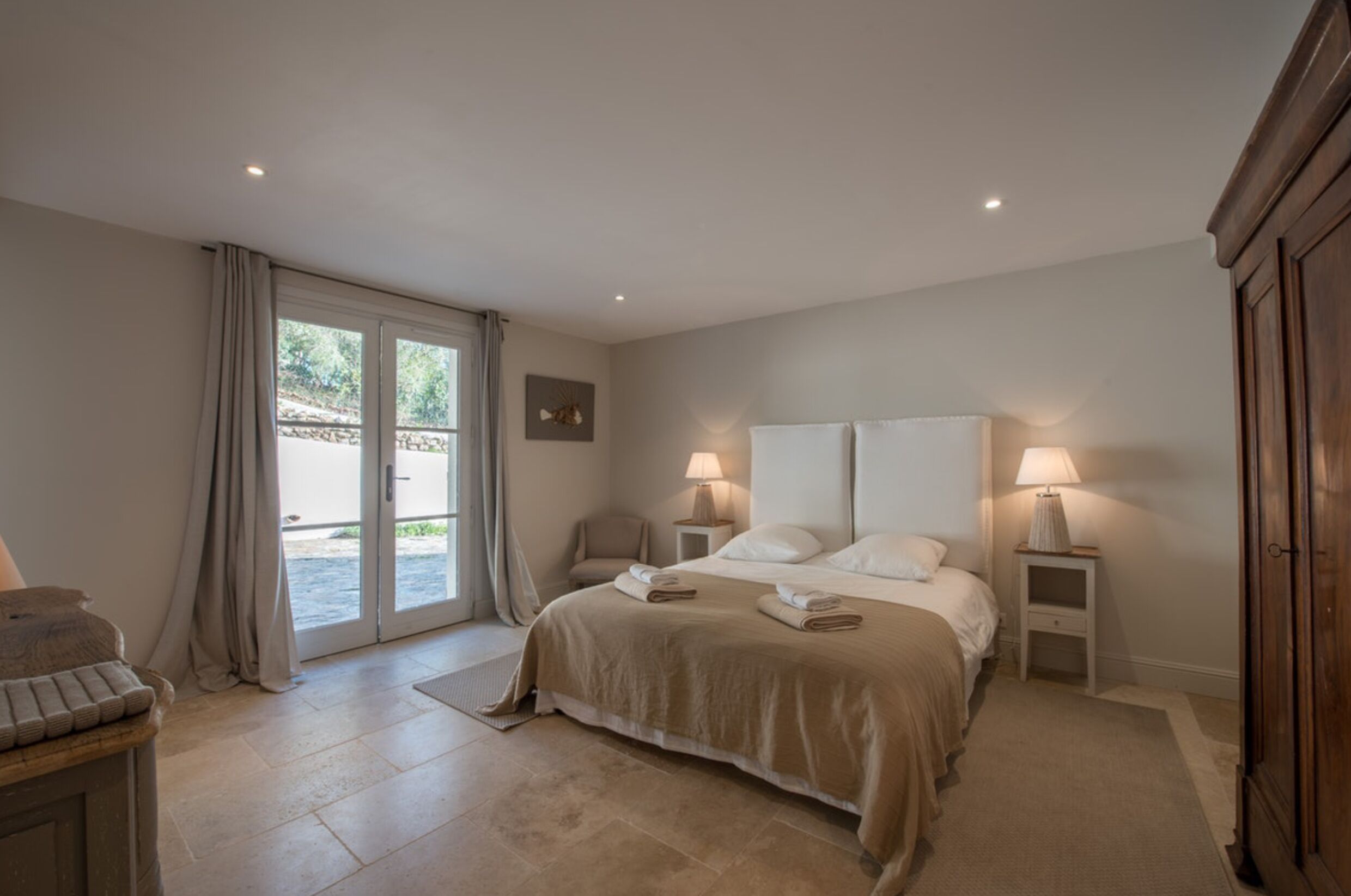 A bedroom with a bed, two bedside tables with lamps, a chair, and a sliding glass door leading to an outdoor area.