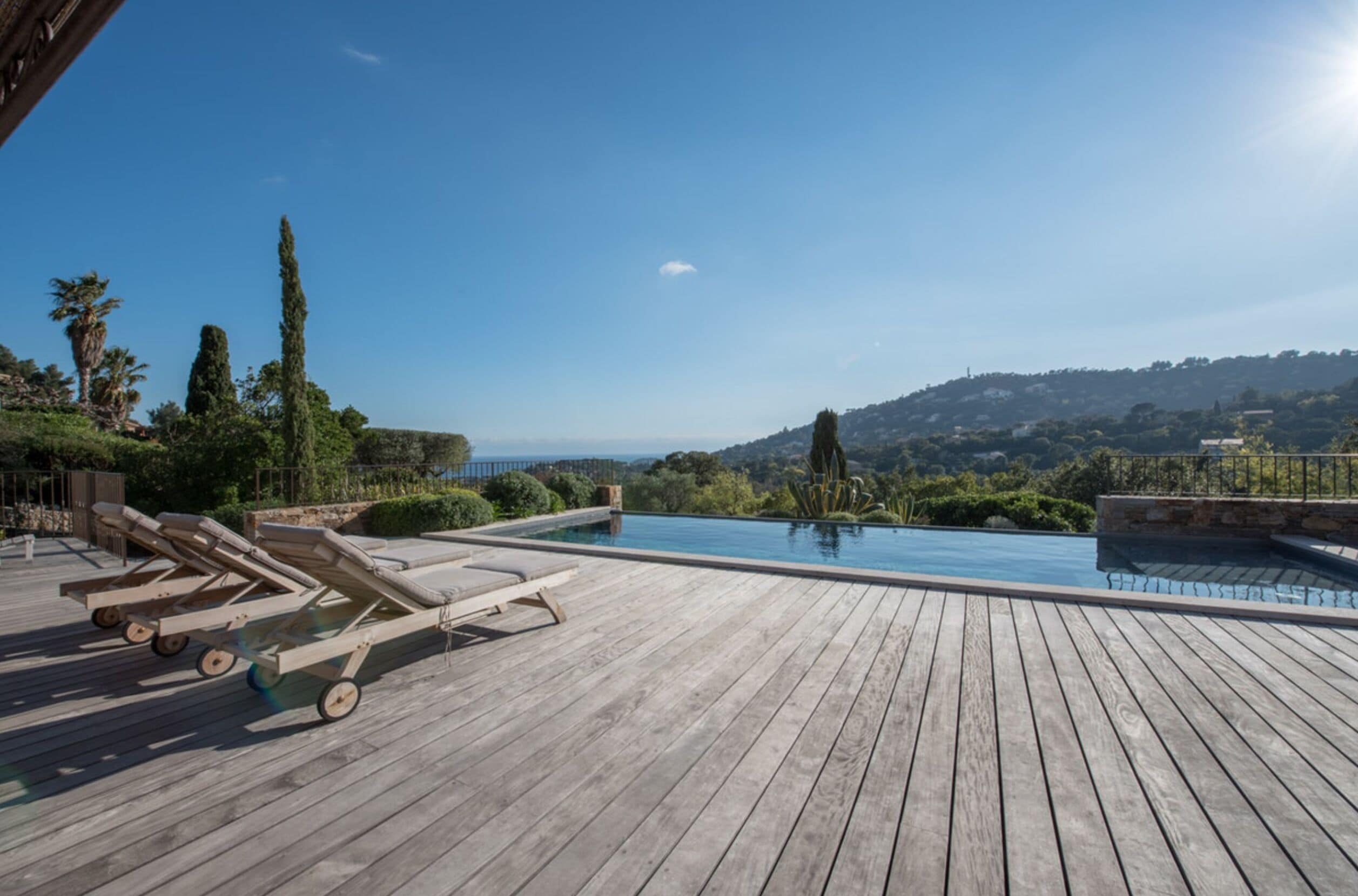 A wooden deck with lounge chairs and a swimming pool overlooking a scenic landscape.