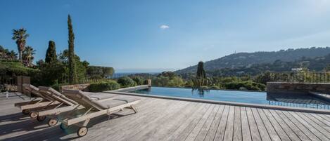 A wooden deck with lounge chairs and a swimming pool overlooking a scenic landscape.