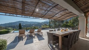 Eine Terrasse im Freien mit einem Holztisch und -stühlen, einem Pool und Blick auf Hügel.