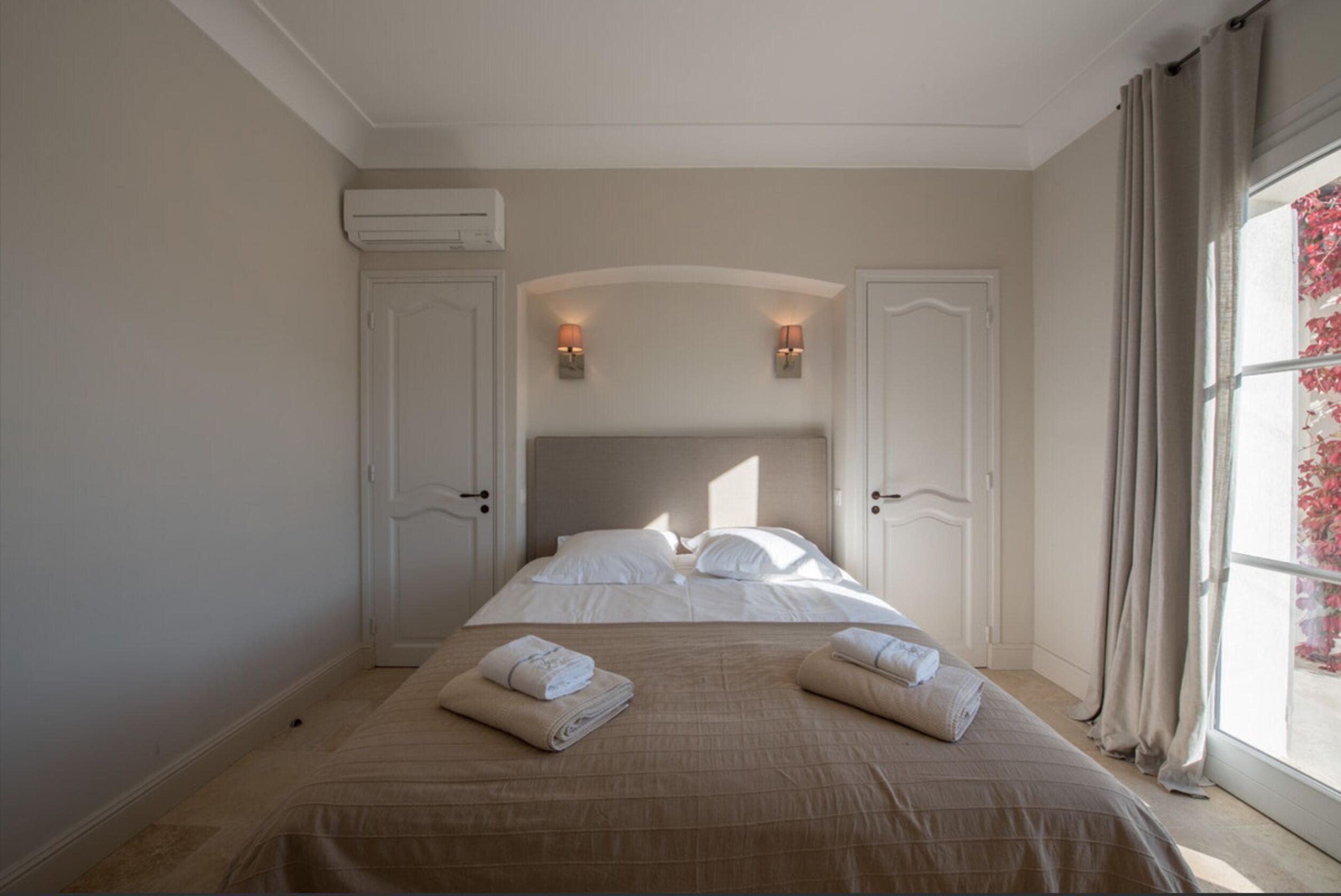 A hotel room with a large bed, two wall-mounted lights, and a window with curtains.