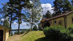 Ein Haus mit gelber Fassade und rotem Dach, umgeben von Bäumen und einer Rasenfläche.