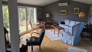 Ein geräumiges Wohnzimmer mit großem Fenster, einer Couch, einem Couchtisch und einem Essbereich mit Korbstühlen.