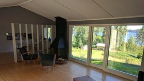 Ein geräumiges Wohnzimmer mit großem Kamin, Holzböden und Blick auf einen See und Wald.