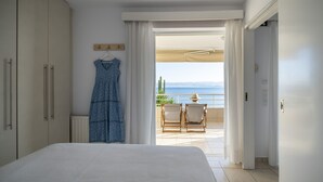 Un dormitorio con cama, armario, un vestido colgado y un balcón con vista al mar.