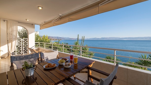 Una mesa de madera con alimentos para el desayuno, una planta en maceta y vistas al mar.